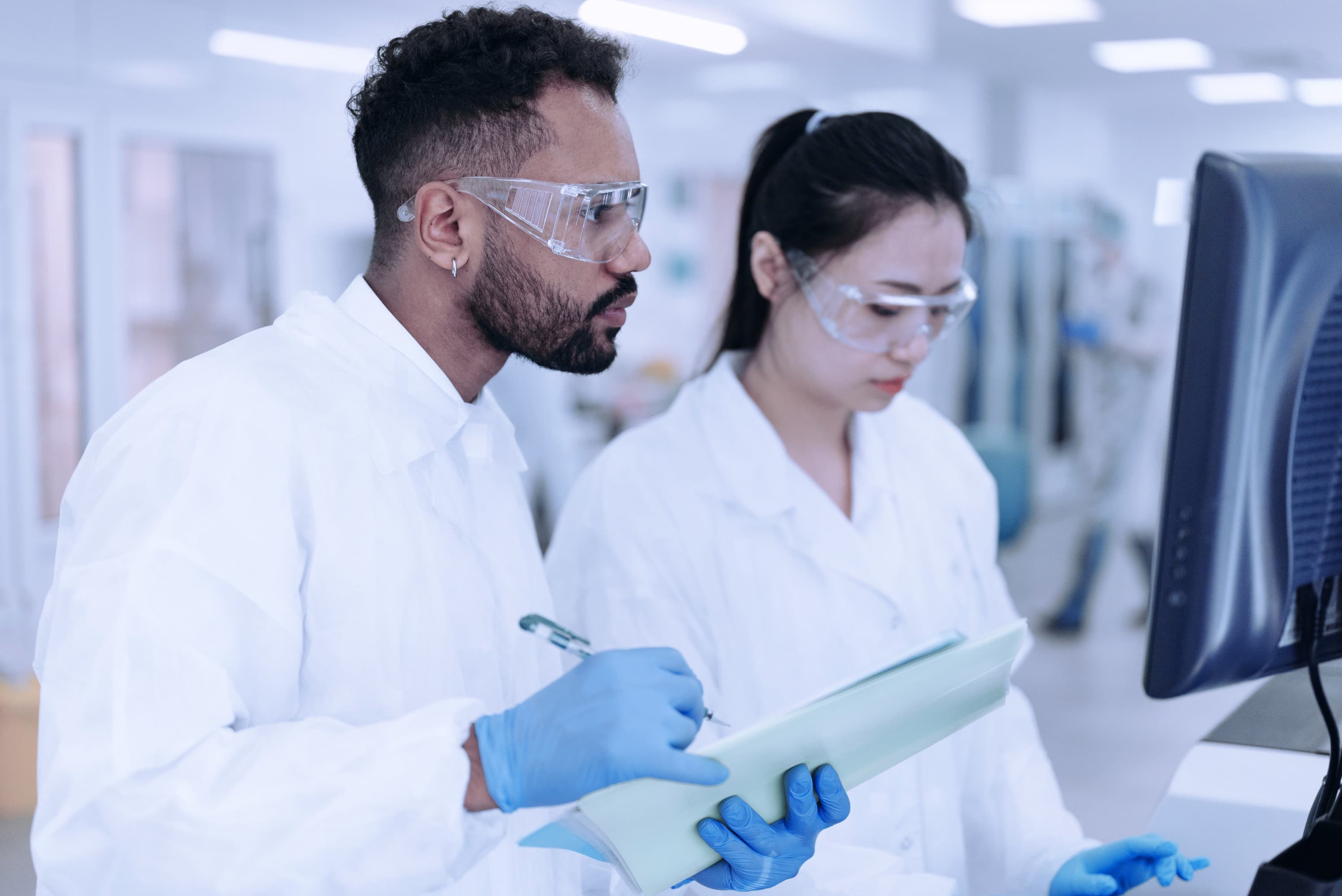 Three semiconductor engineers in cleanroom suits collaborating in a fabrication facility